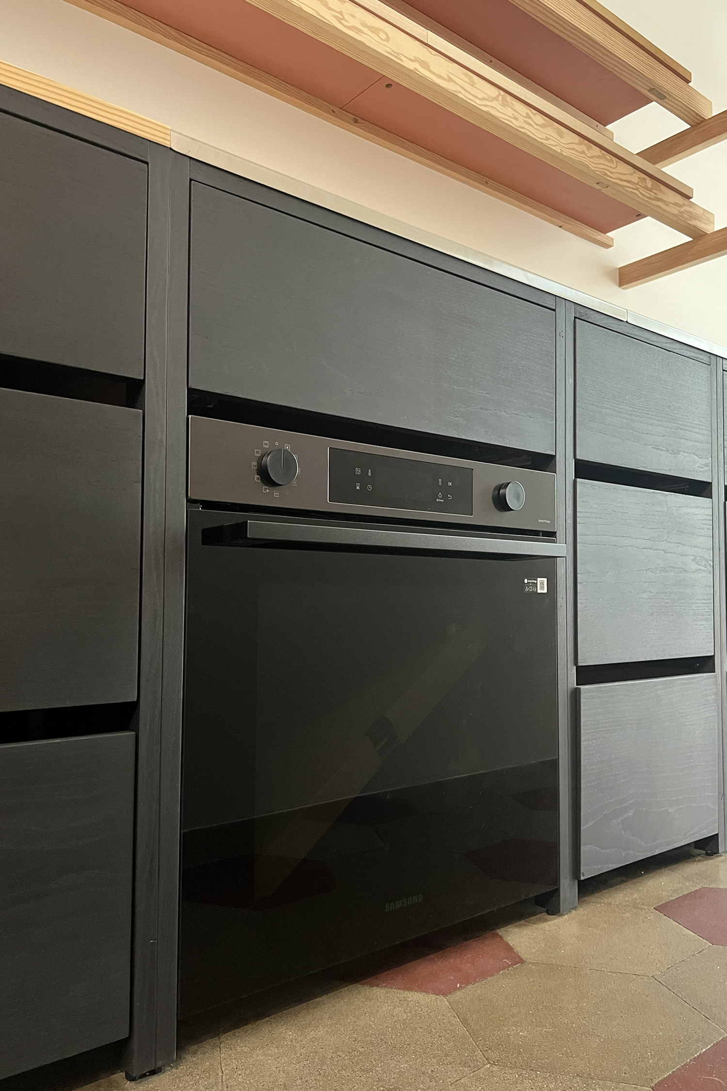 Cucina su misura con basi nere, forno integrato e mensole in legno