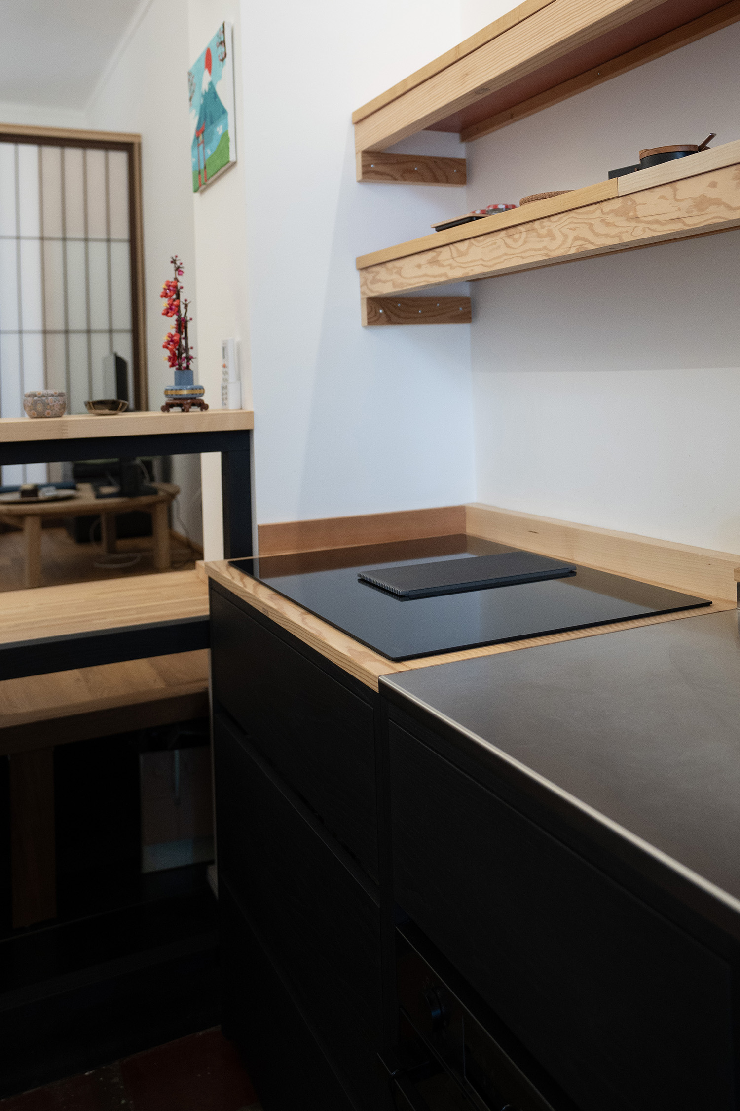 Vista laterale della cucina su misura con basi nere, piano in legno, piano cottura induzione e mensole a parete