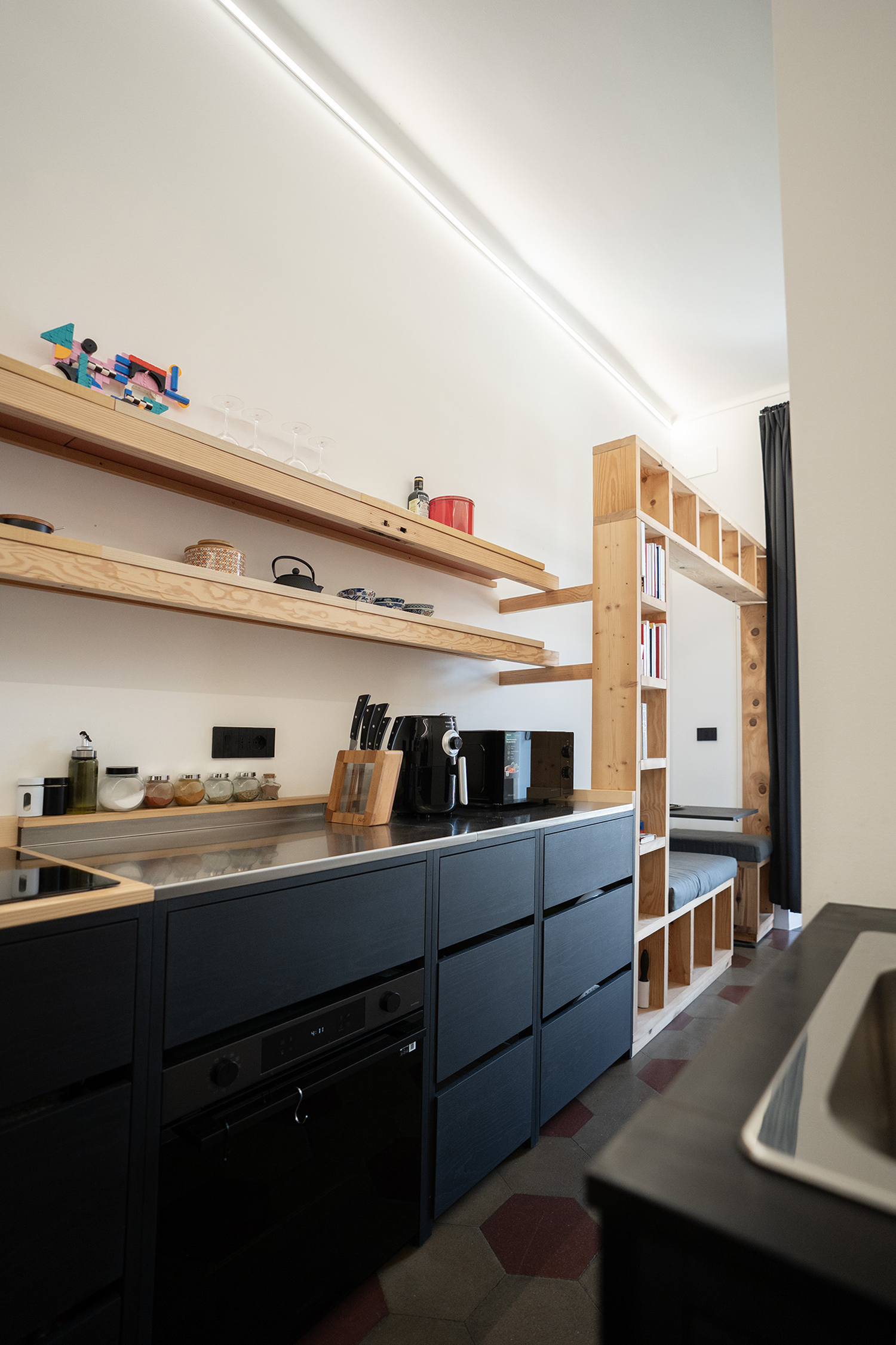 Vista generale della cucina su misura con basi nere, piano in legno e mensole a parete